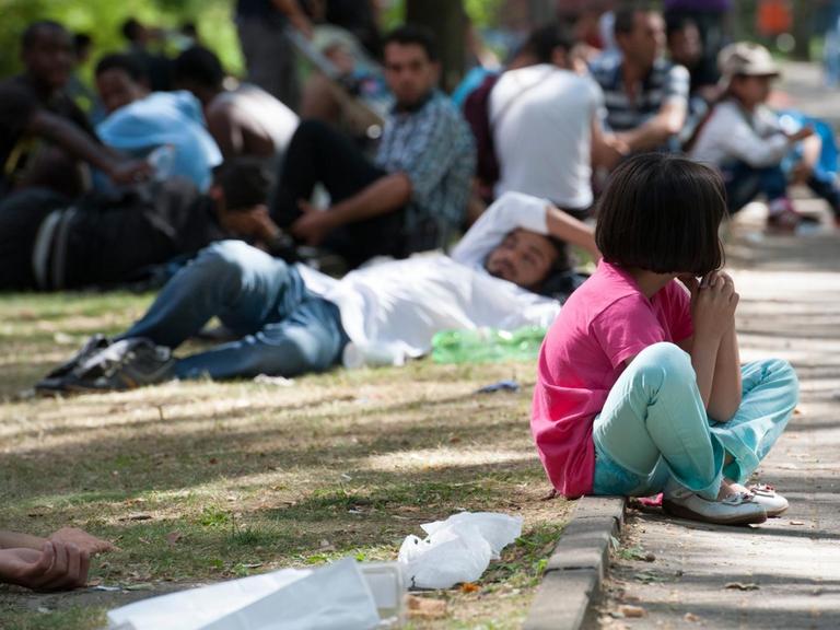 Ein Flüchtlingskind sitzt in Berlin auf dem Gelände des Landesamtes für Gesundheit und Soziales (LaGeSo) auf einem Bordstein.