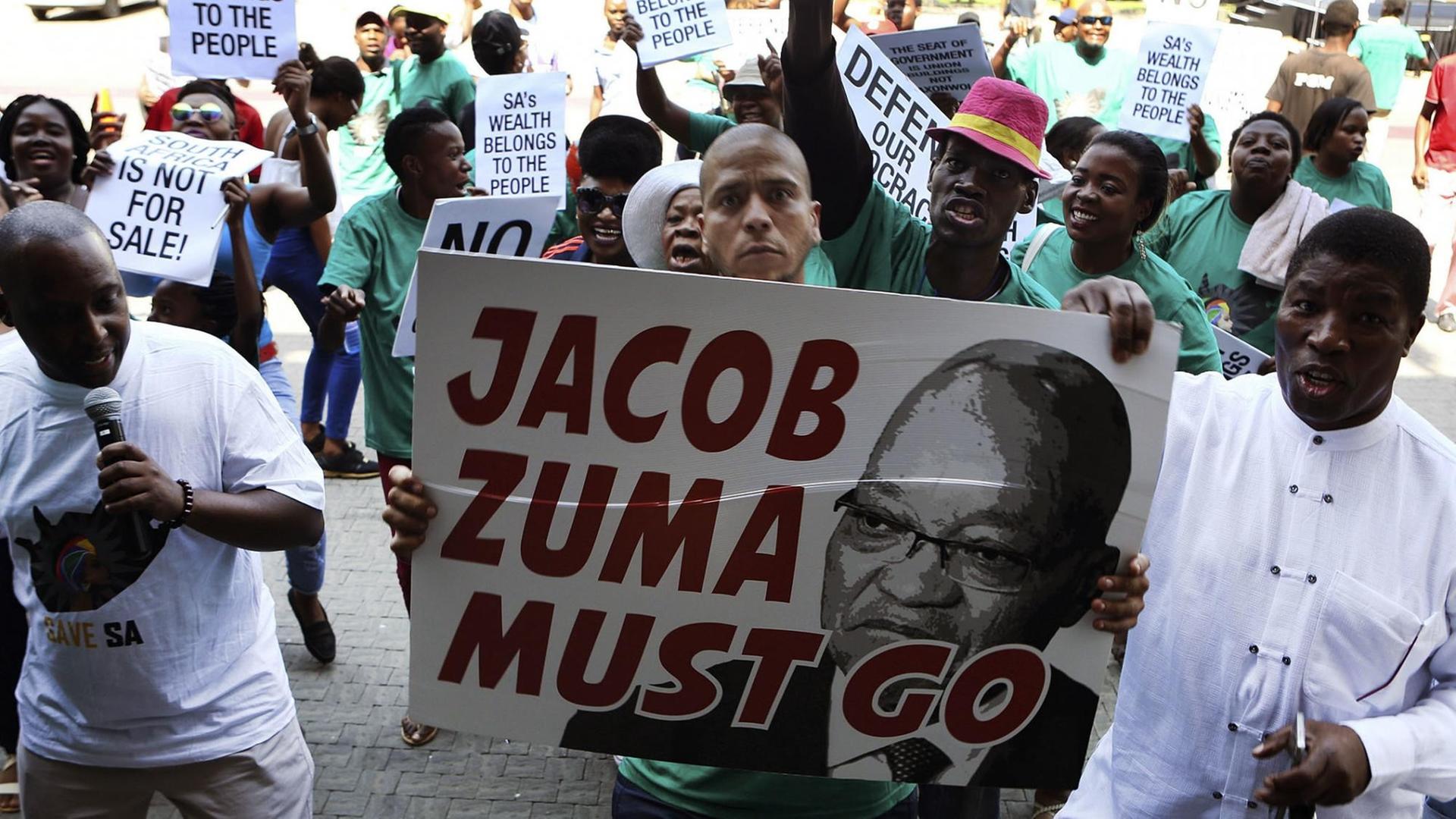 Demonstranten protestieren gegen den südafrikanischen Präsidenten Jacob Zuma; auf einem Transparent steht "Zuma must go".
