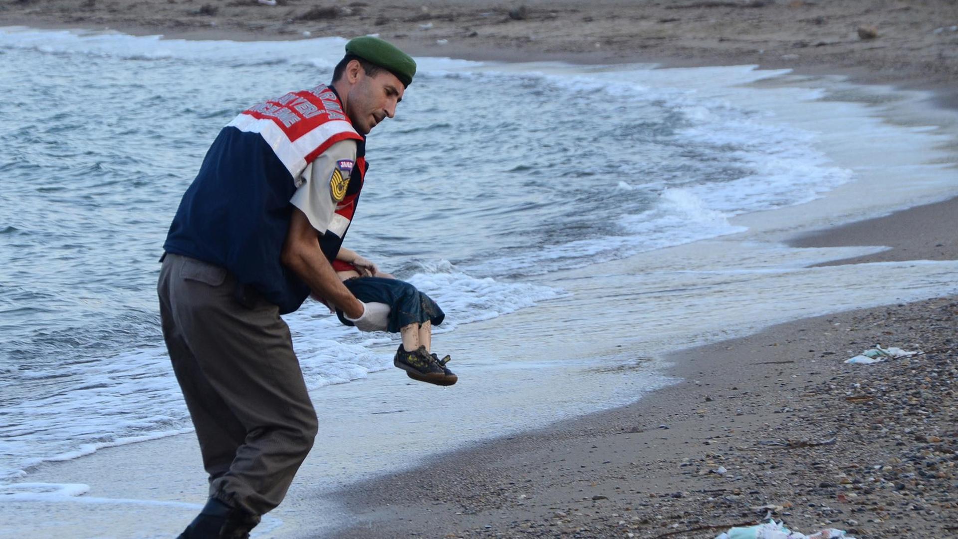 Ein türkischer Polizist trägt ein totes Kind im Arm und bringt es vom Strand weg. Der Oberkörper des Kindes wird vom Körper des Polizisten verdeckt.. Ein türkischer Polizist trägt ein totes Kind im Arm und bringt es vom Strand weg. Der Oberkörper des Kindes wird vom Körper des Polizisten verdeckt..