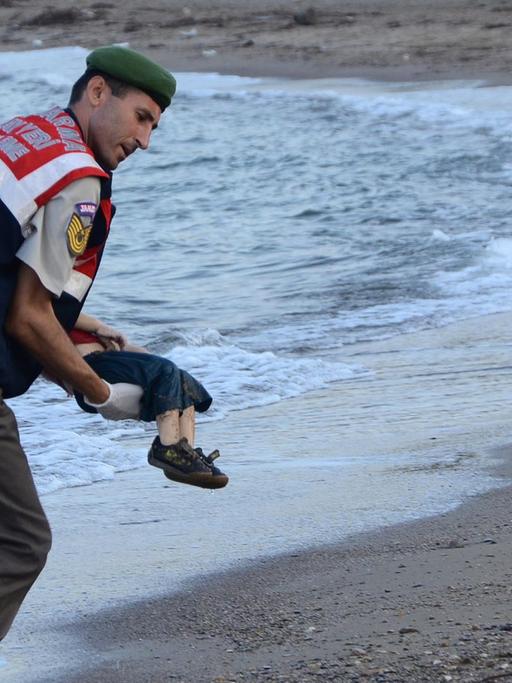 Ein türkischer Polizist trägt ein totes Kind im Arm und bringt es vom Strand weg. Der Oberkörper des Kindes wird vom Körper des Polizisten verdeckt..