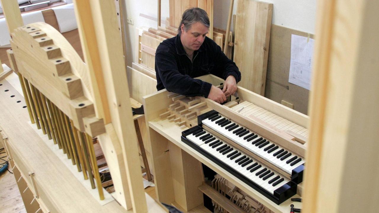 Ein Mann steht schraubend an einem Holzkasten, an dem zwei Tastaturen montiert sind. Ein Mann steht schraubend an einem Holzkasten, an dem zwei Tastaturen montiert sind.