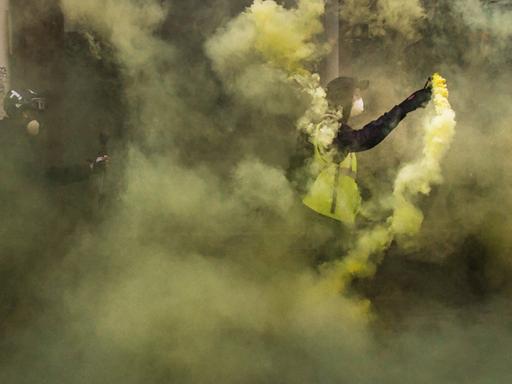 Zwei Männer, einer in einer gelben Warnweste, stehen im gelblichen Rauch von gezündeter Pyrotechnik.