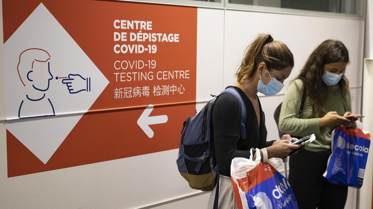 Frauen am Flughafen Roissy Charles de Gaulle bei Paris neben einem Hinweisschild für eine Corona-Teststation Frauen am Flughafen Roissy Charles de Gaulle bei Paris neben einem Hinweisschild für eine Corona-Teststation
