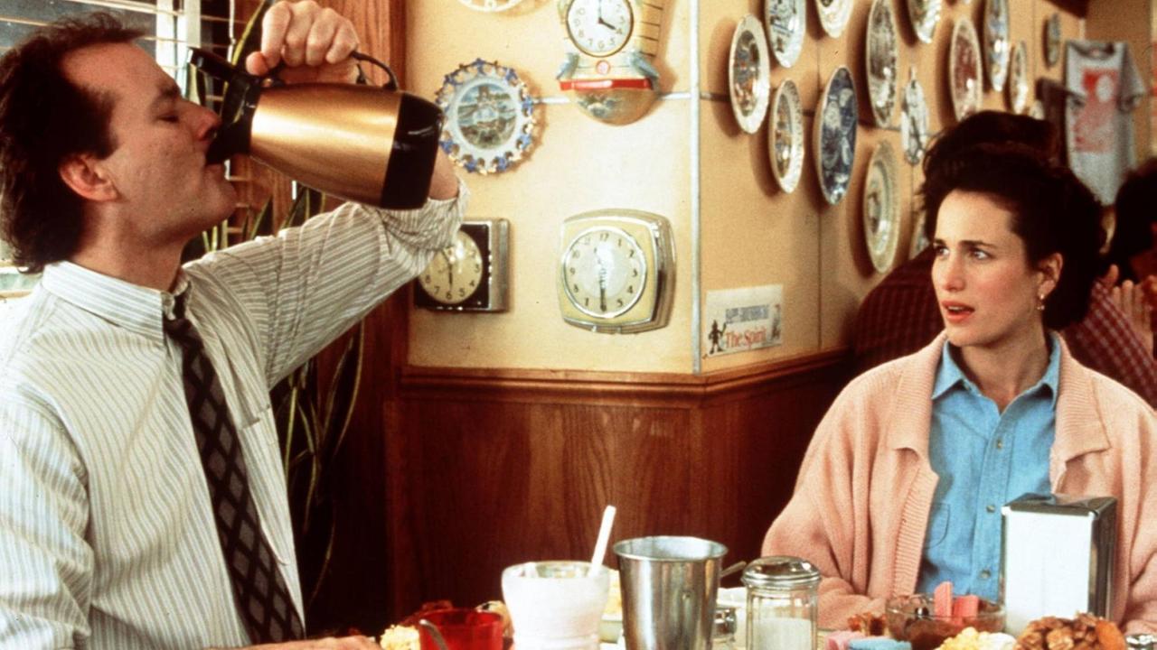 Der Meteorologe Phil, gespielt von Bill Murray, sitzt neben seiner Aufnahmeleiterin Rita Hanson, gespielt von Andie MacDowell, an einem Tisch und trinkt Kaffee direkt aus einer Kaffeekanne. Der Meteorologe Phil, gespielt von Bill Murray, sitzt neben seiner Aufnahmeleiterin Rita Hanson, gespielt von Andie MacDowell, an einem Tisch und trinkt Kaffee direkt aus einer Kaffeekanne.