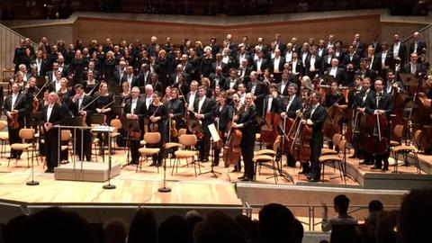 Ein Orchester und ein Chor nehmen mit einem Dirigenten den Beifall des Publikums in der Berliner Philharmonie an.