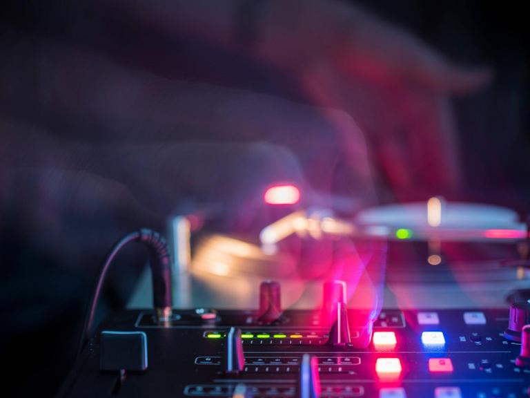 DJ-Hände an einem Mischpult mit farbigen Lichtstrahlen in Club-Atmosphäre