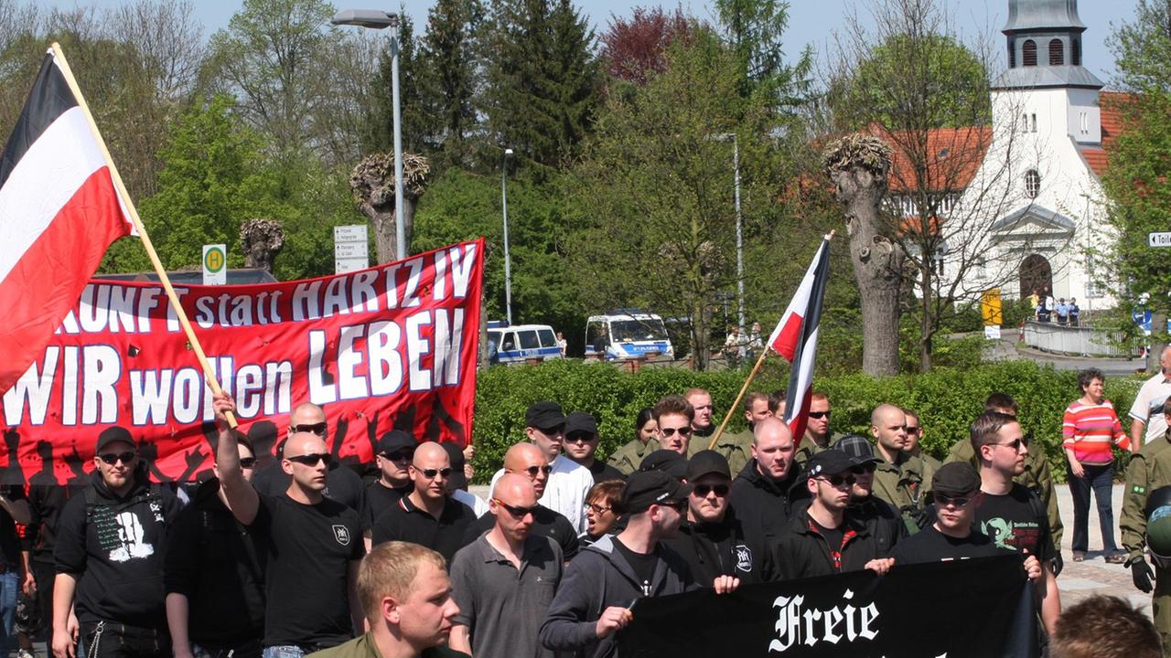 Rund 120 Neonazis laufen in Wittstock (Brandenburg) mit Bannern und Fahnen. Im Hintergrund ist eine Kirche zu sehen.
