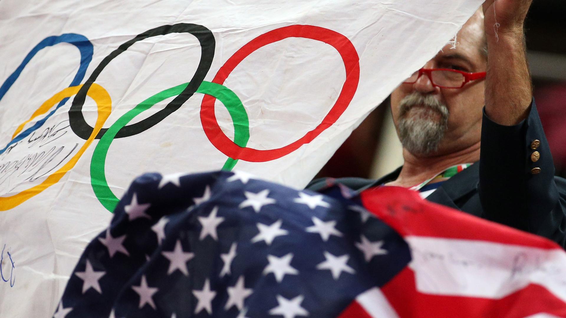 Ein Mann hält die Olympische Flagge und die der USA in die Höhe.