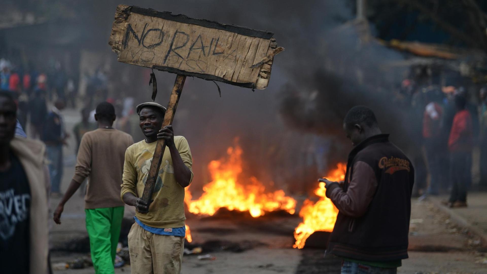 Ein Demonstrant steht in Nairobi neben einer brennenden Barrikade und hält ein Schild mit der Aufschrift: "Kein Raila, kein Frieden".