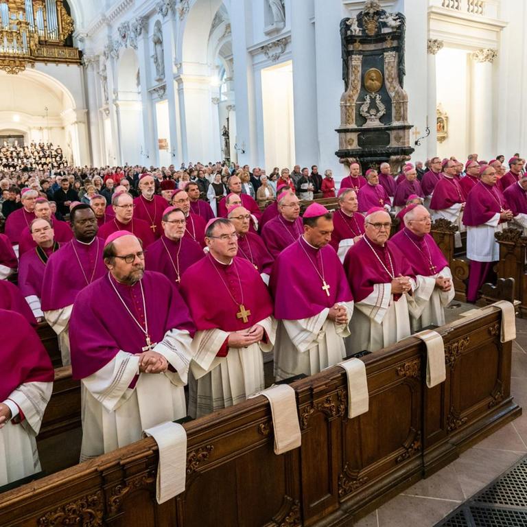 Dutzende Bischöfe stehen in violetten Gewändern in den Gebetsbänken.