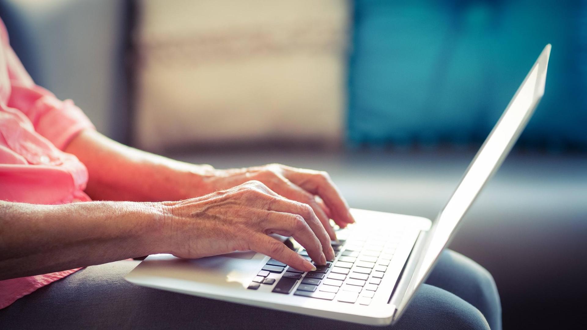 Eine ältere Frau hat einen Laptop auf dem Schoss und tippt darauf Eine ältere Frau hat einen Laptop auf dem Schoss und tippt darauf
