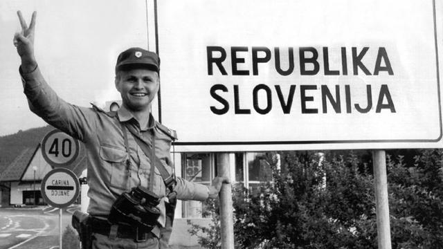 Ein slowenischer Soldat steht in Lavamünd neben einem neu errichteten Schild an der Grenze von Österreich nach Slowenien mit der Aufschrift "Republika Slovenija" und macht das Siegeszeichen, aufgenommen am 29. Juni 1991.