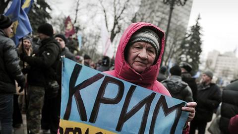 Eine Frau hält ein Schild in den Farben der ukrainischen Flagge mit der Aufschrift "Krim - Sevastopol" in Händen.