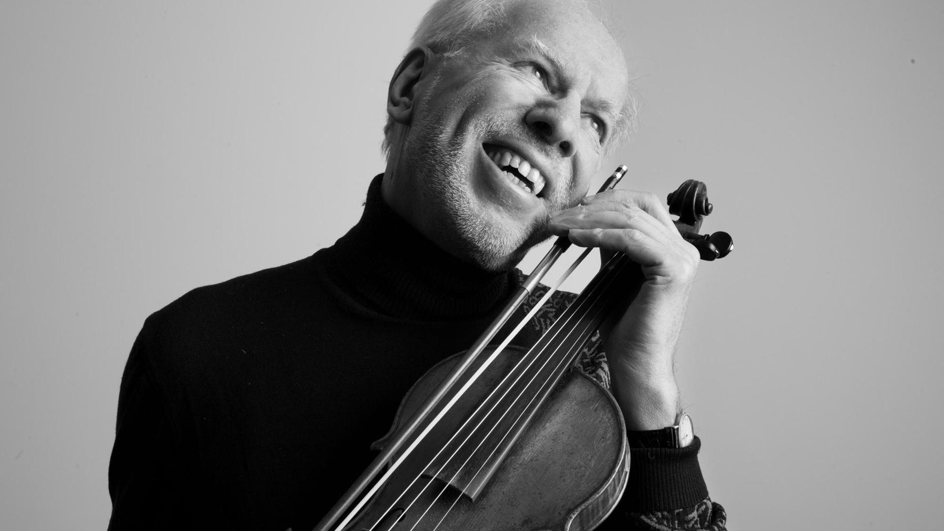 Ein Mann hält sein Gesicht lachend an das Griffbrett einer Violine. Ein Mann hält sein Gesicht lachend an das Griffbrett einer Violine.
