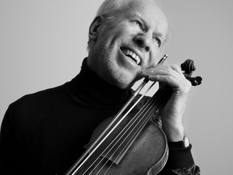 Ein Mann hält sein Gesicht lachend an das Griffbrett einer Violine.