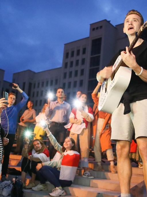 Ein junger Gitarrist gibt in Minsk abends auf einen Platz ein spontanes Konzert. Das Publikum macht Fotos, einige haben sich in die belarusische Fahne gewickelt. Valery Sharifulin/TASS PUBLICATIONxINxGERxAUTxONLY TS0E4073