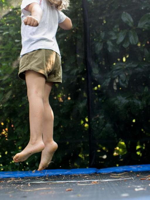 Ein Mädchen springt in einem Garten auf einem Trampolin.