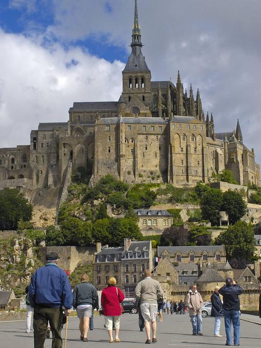Touristen laufen auf einer Straße auf den Ort Mont-Saint-Michel mit der Abtei in der Normandie in Frankreich zu.