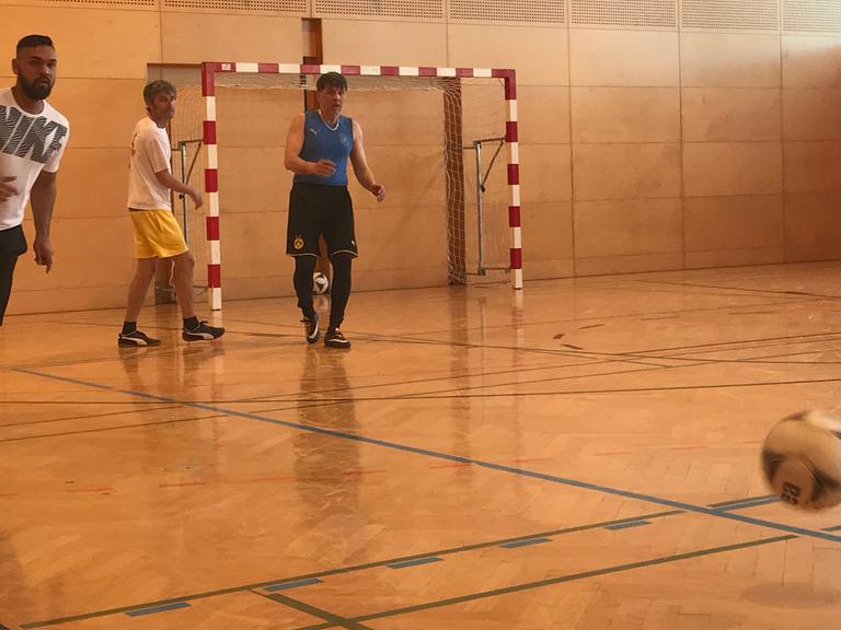Die Spieler des "FC International" spielen in einer Turnhalle Fußball.