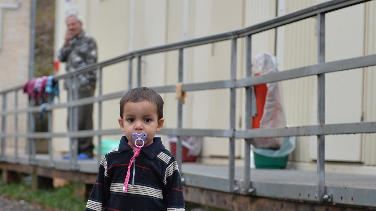 Ein Kleinkind steht am 21.11.2013 in Eisenberg (Thüringen) auf dem Gelände der Erstaufnahmestelle für Flüchtlinge und Asylbewerber vor Wohncontainern. Die Suche nach einer neuen Erstaufnahmestelle für Flüchtlinge in Thüringen gestaltet sich weiterhin schwierig. Es sei noch keine Entscheidung gefallen, sagte ein Sprecher des Innenministeriums der Nachrichtenagentur dpa in Erfurt. Ein Kleinkind steht am 21.11.2013 in Eisenberg (Thüringen) auf dem Gelände der Erstaufnahmestelle für Flüchtlinge und Asylbewerber vor Wohncontainern. Die Suche nach einer neuen Erstaufnahmestelle für Flüchtlinge in Thüringen gestaltet sich weiterhin schwierig. Es sei noch keine Entscheidung gefallen, sagte ein Sprecher des Innenministeriums der Nachrichtenagentur dpa in Erfurt.