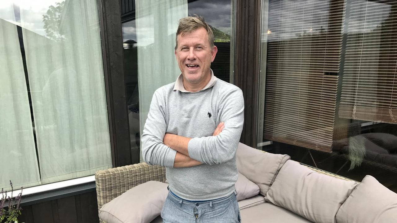 Ein Mann in Jeans und Sweater steht mit verschränkten Armen vor einer Sofagarnitur auf der Terrasse. Ein Mann in Jeans und Sweater steht mit verschränkten Armen vor einer Sofagarnitur auf der Terrasse.