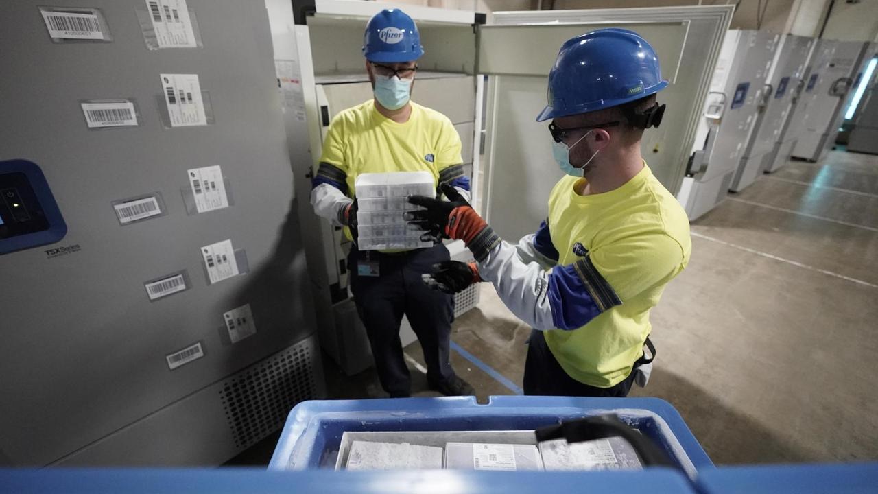 Mitarbeiter mit Mundschutz und Helmen verladen Kisten Mitarbeiter mit Mundschutz und Helmen verladen Kisten
