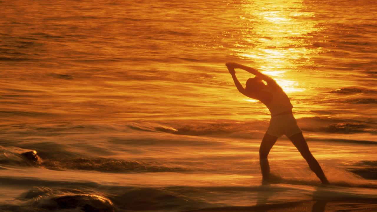 Eine Frau entspannt sich bei Yoga-Übungen im Licht der untergehenden Sonne an einem Strand in Kalifornien.