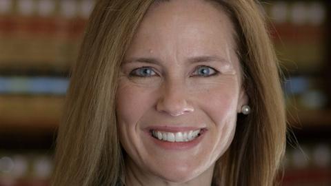 Ein Portrait von Bundesrichterin Amy Coney Barrett. Sie hat offenes, dunkelblondes Haar, blaugraue Augen und leichte Grübchen-Falten auf beiden Wangen.