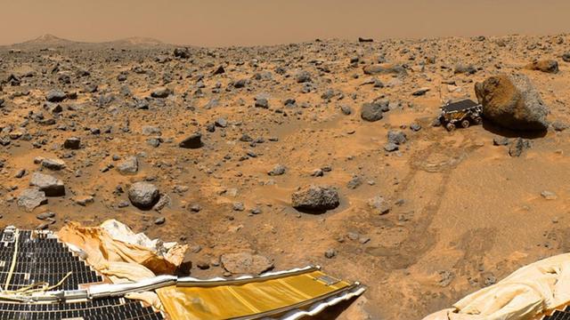 Der Marsrover Sojourner erkundet einen Felsbrocken; im Vordergrund ein Teil der Pathfinder-Sonde.
