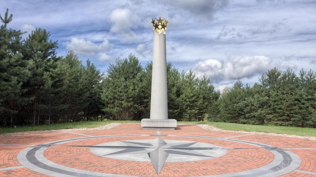 Der genaue Ort der geografischen Mitte Europas in Purnuskes, Litauen. Eine graue Säule mit goldenen Sternen auf der Spitze steht auf sternförmig angeordneten Pflastersteinen.