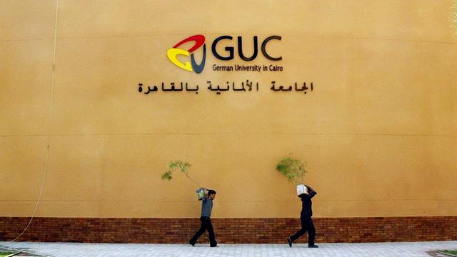 Arbeiter tragen Topfpflanzen am Auditorium der Deutschen Universität in Kairo am vorbei.
