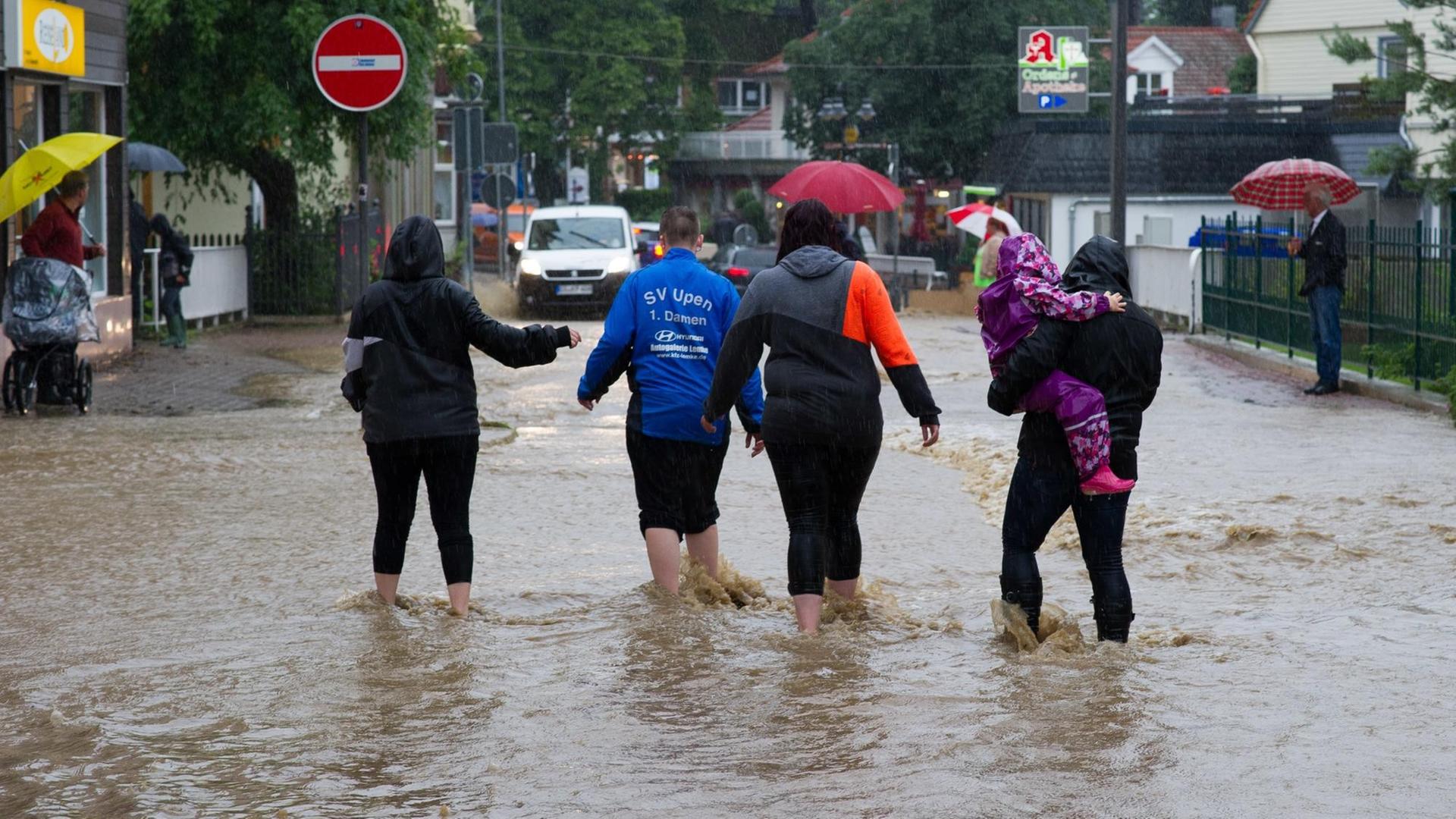Passanten gehen am 26.07.2017 in Bad Harzburg (Niedersachsen) durch Wasser einer überfluteten Straße. Dauerregen hat im südlichen Niedersachsen in einigen Orten zu Überschwemmungen geführt. Passanten gehen am 26.07.2017 in Bad Harzburg (Niedersachsen) durch Wasser einer überfluteten Straße. Dauerregen hat im südlichen Niedersachsen in einigen Orten zu Überschwemmungen geführt.