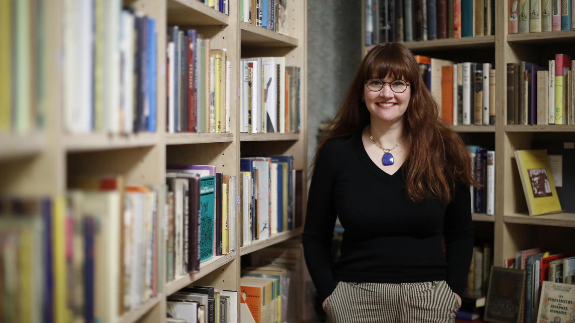 Allison Devers steht in ihrem Buchladen "Second Shelf" in London, umgeben von gefüllten Bücherregalen und lächelt in die Kamera, die Hände in den Hosentaschen. Allison Devers steht in ihrem Buchladen "Second Shelf" in London, umgeben von gefüllten Bücherregalen und lächelt in die Kamera, die Hände in den Hosentaschen.