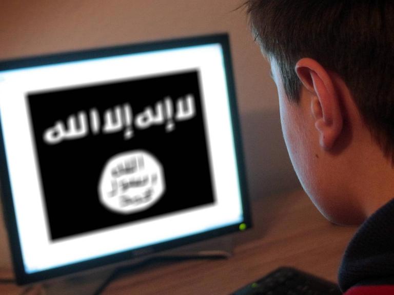 Ein Jugendlicher sitzt am Bildschirm eines PCs, der die Flagge der Terrormiliz IS zeigt.