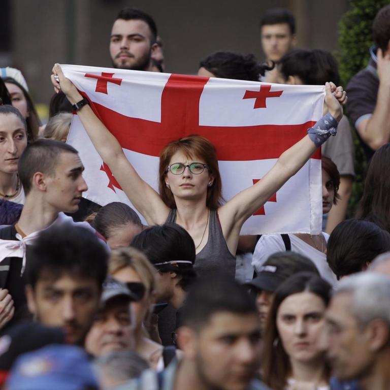 Im Zentrum der Menschenmenge steht eine Frau mit Brille, die eine georgische Flagge hochhält. 