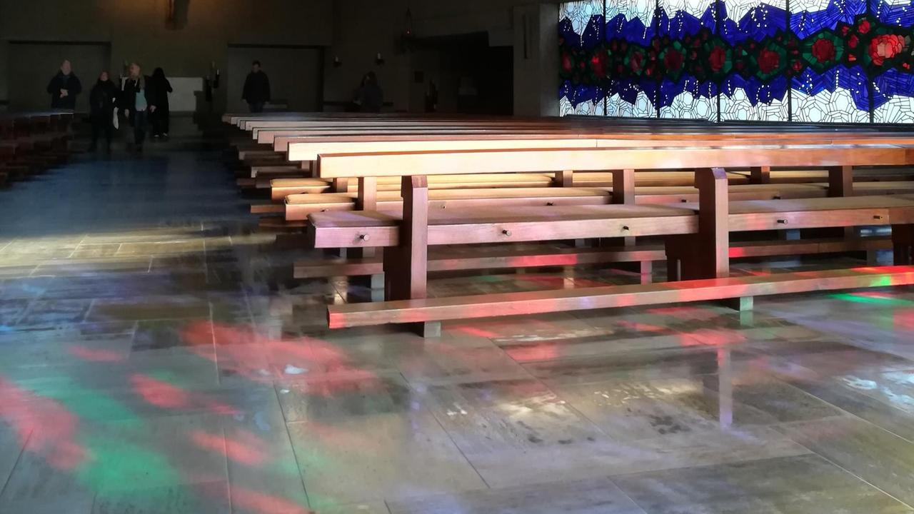 Das Foto zeigt den Innenraum der Frankfurter Kirche St. Ignatius des Kirchenbaumeisters Gottfried Böhm. Lichtreflexe von den bunten Betonglasfenstern sind auf Boden und Kirchenbänken zu sehen. Das Foto zeigt den Innenraum der Frankfurter Kirche St. Ignatius des Kirchenbaumeisters Gottfried Böhm. Lichtreflexe von den bunten Betonglasfenstern sind auf Boden und Kirchenbänken zu sehen.