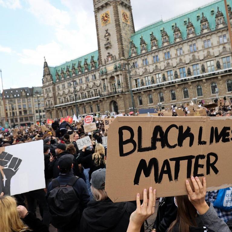 Teilnehmer einer Demonstration gegen Rassismus und Polizeigewalt protestieren mit einem Schild mit der Aufschrift "Black Lives Matter" auf dem Rathausmarkt in Hamburg.