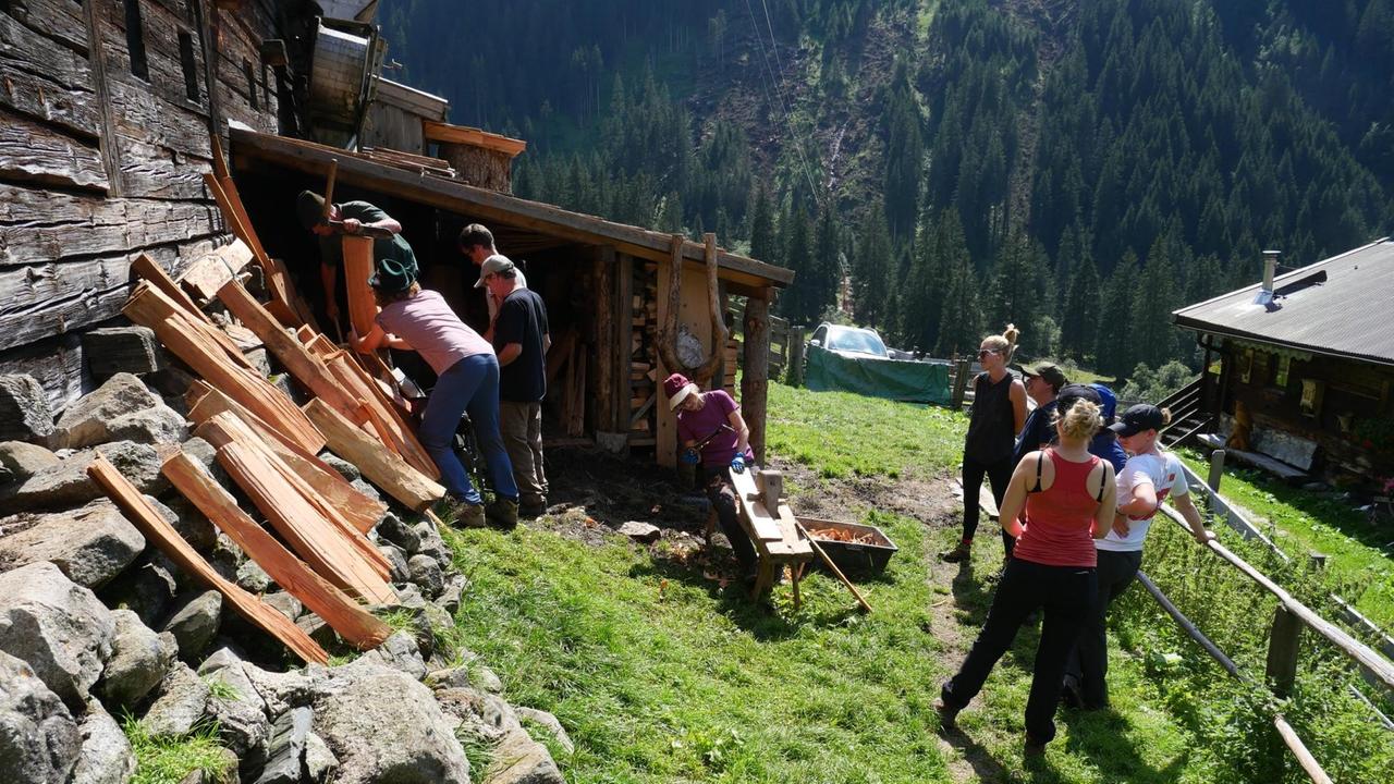 Männer mit Werkzeug bearbeiten Holzbretter, die an die Wand einer Berghütte gelehnt sind. Männer mit Werkzeug bearbeiten Holzbretter, die an die Wand einer Berghütte gelehnt sind.