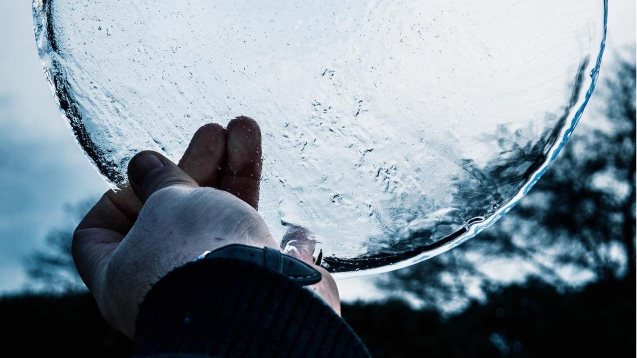 Eine Hand hält eine runde Eis-Scheibe gegen den Himmel.
