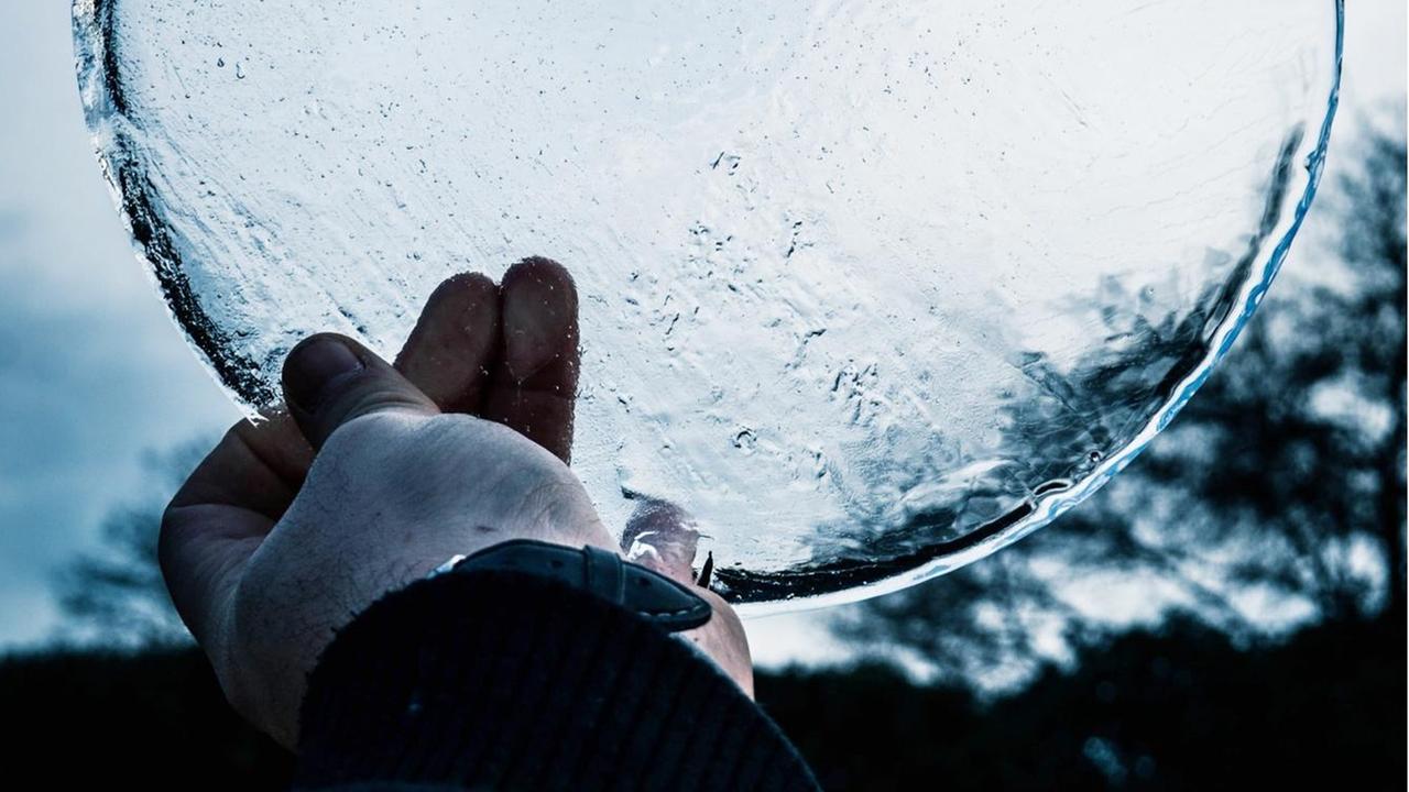 Eine Hand hält eine runde Eis-Scheibe gegen den Himmel. Eine Hand hält eine runde Eis-Scheibe gegen den Himmel.