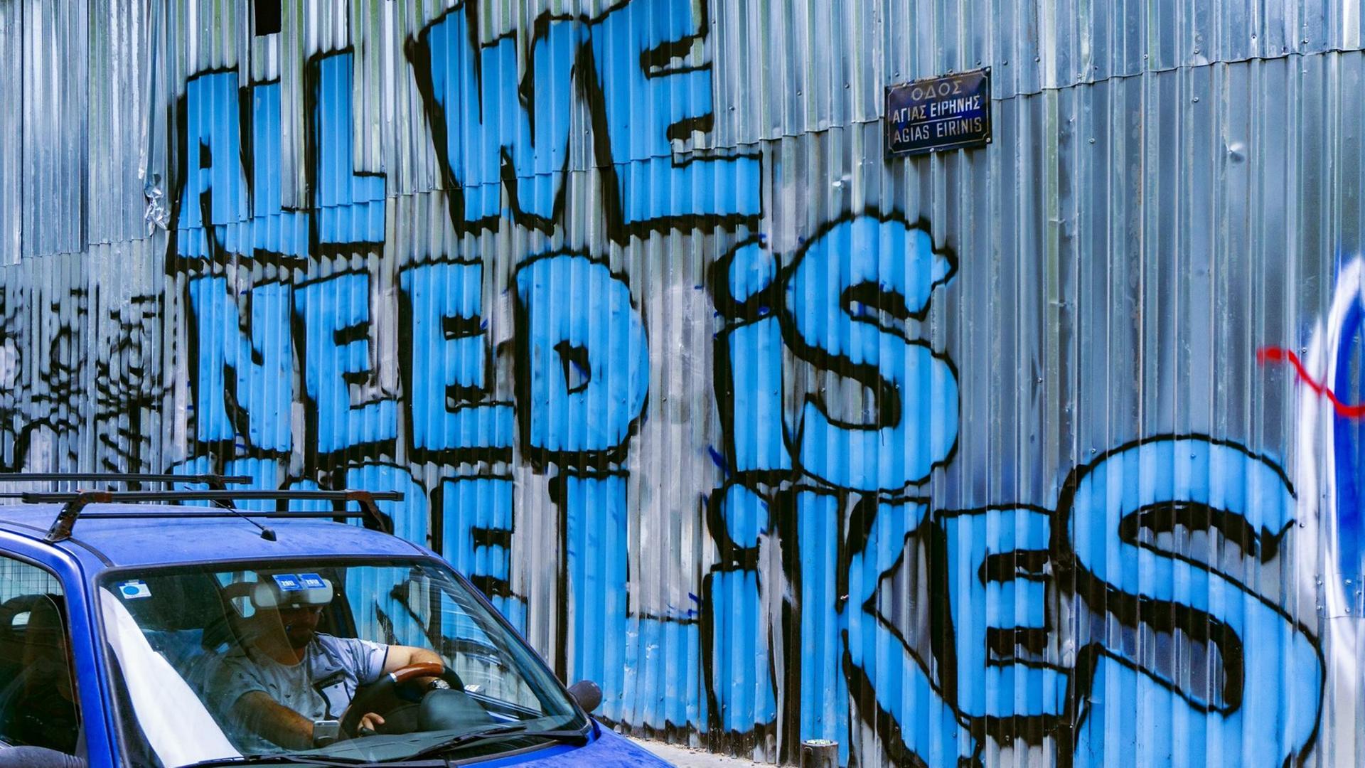 Ein Auto passiert eine Wellblechwand mit einem Graffiti, das in großer blauer Schrift verkündet: "All We Need Is More Likes".