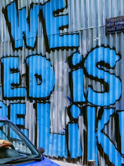 Ein Auto passiert eine Wellblechwand mit einem Graffiti, das in großer blauer Schrift verkündet: "All We Need Is More Likes".