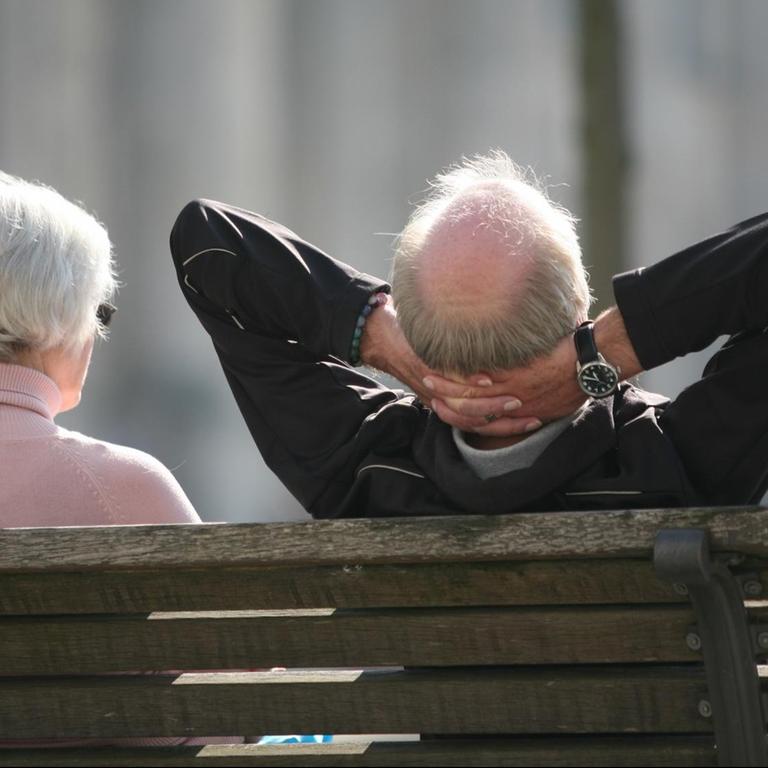 Ein Rentnerpaar sitzt auf einer Bank vor dem Reichstag und sonnt sich