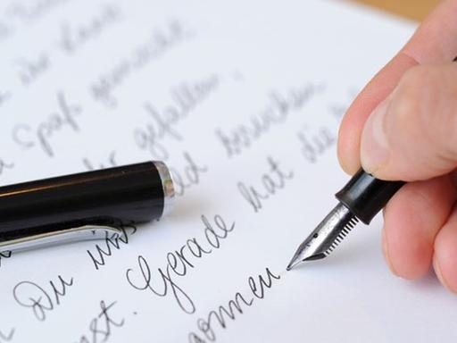 Die Hand einer Frau, die einen Brief mit einem Füllfederhalter schreibt.