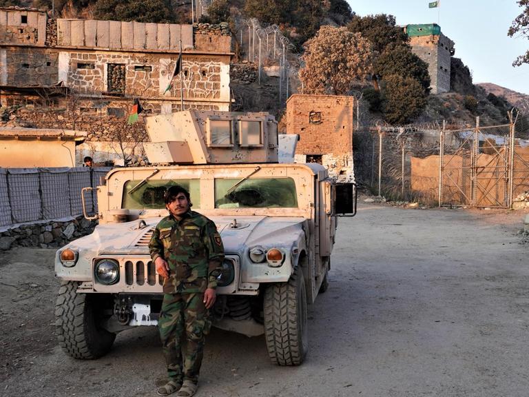 Ein Grenzposten in der afghanischen Provinz Kunar an der Grenze zu Pakistan. Er lehnt vor einem Militärfahrzeug. Hinter ist der Grenzzaun.
