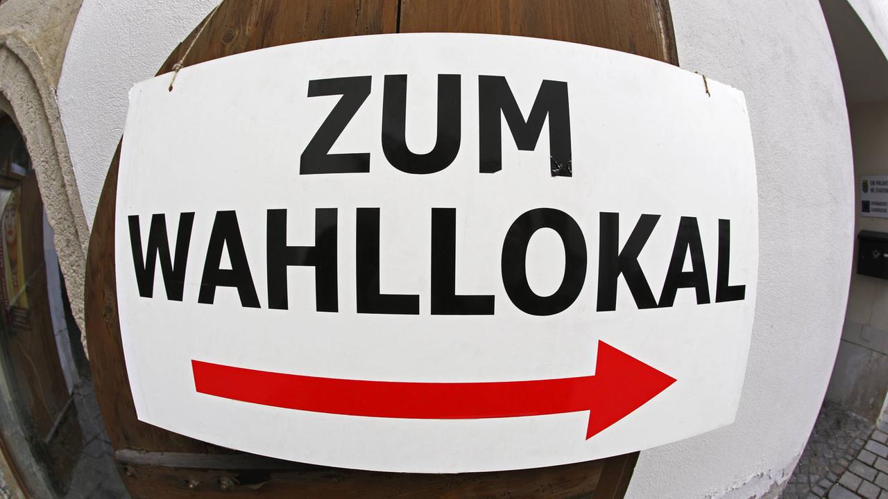 Auf einem Schild steht "Zum Wahllokal", darunter ein roter Pfeil. Auf einem Schild steht "Zum Wahllokal", darunter ein roter Pfeil.