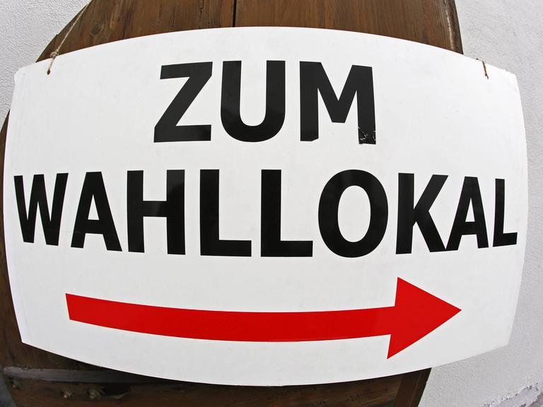 Auf einem Schild steht "Zum Wahllokal", darunter ein roter Pfeil.