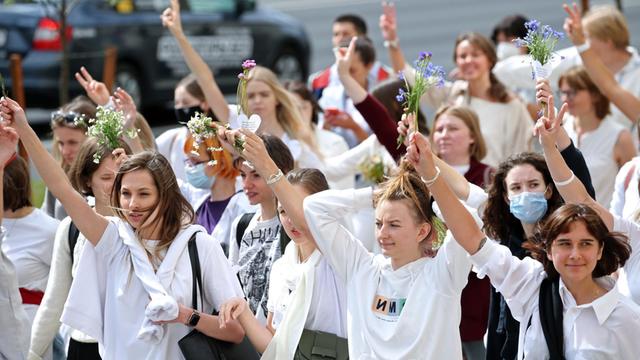 Junge Frauen demonstrieren. Sie tragen weiße Kleidung und halten Blumen in den Händen.