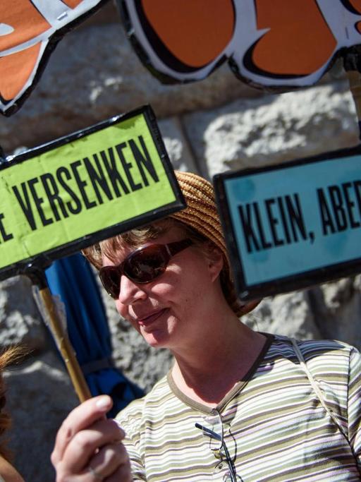 Eine Aktivistin der Initiative "Deutsche Wohnen & Co enteignen" nimmt mit selbstgebastelten Schildern, afu dem "Miethaie versenken" und "Klein, aber Gemeinwohl" steht, an der Übergabe von 77.001 Unterschriften zur Anstrebung eines Volksbegehrens an die Berliner Senatsverwaltung für Inneres und Sport teil.