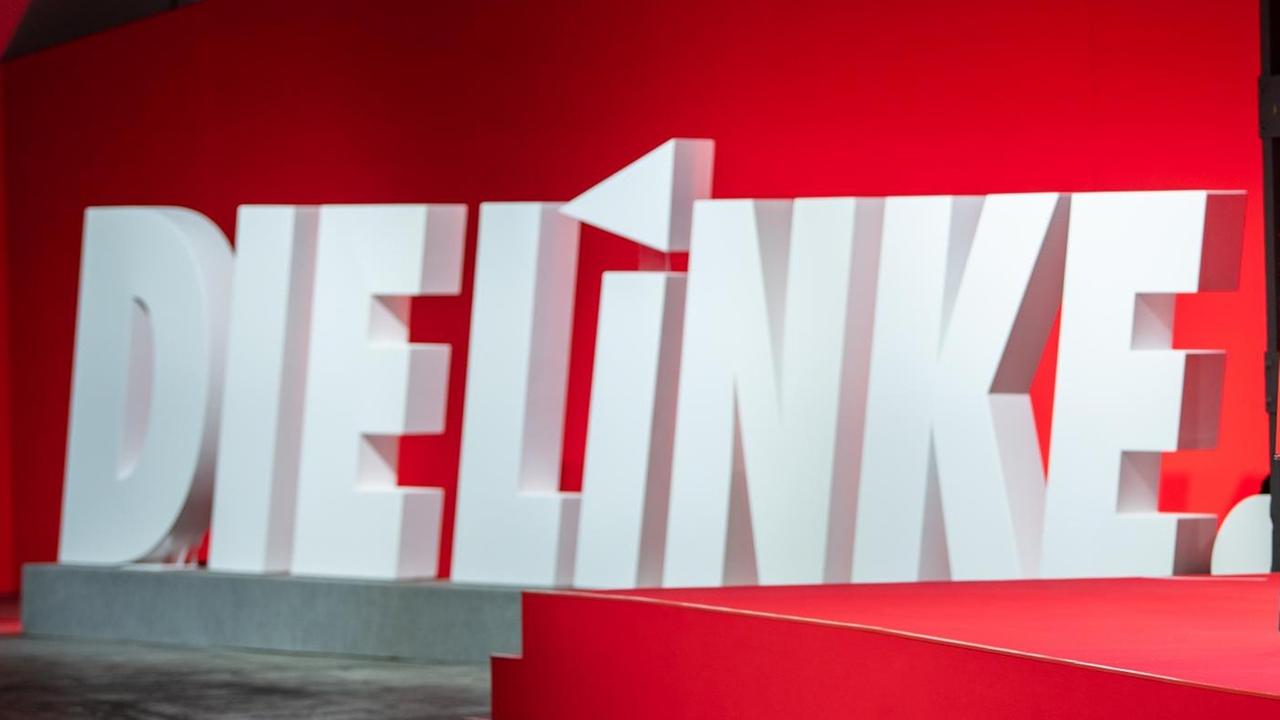 Die Worte "Die Linke" stehen in weiß auf rotem Grund hinter einem Rednerpult. Die Worte "Die Linke" stehen in weiß auf rotem Grund hinter einem Rednerpult.